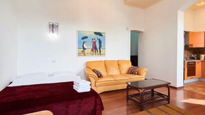 A living room with a bed, a yellow sofa, a wooden coffee table, and a painting on the wall. - Home-Hotel Khoriva 15 (Kyiv)