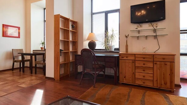 A spacious room with a wooden desk, a chair, a bookshelf, a TV mounted on the wall, and a window providing natural light. - Home-Hotel Khoriva 15 (Kyiv)