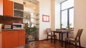 A compact kitchen with orange cabinets, a microwave, and a dining area with two chairs and a table. - Home-Hotel Khoriva 15 (Kyiv)
