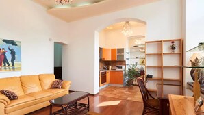 A living room with a sofa, coffee table, and wooden floor. There is a kitchen in the background with orange cabinets and a dining area with a wooden table. - Home-Hotel Khoriva 15 (Kyiv)