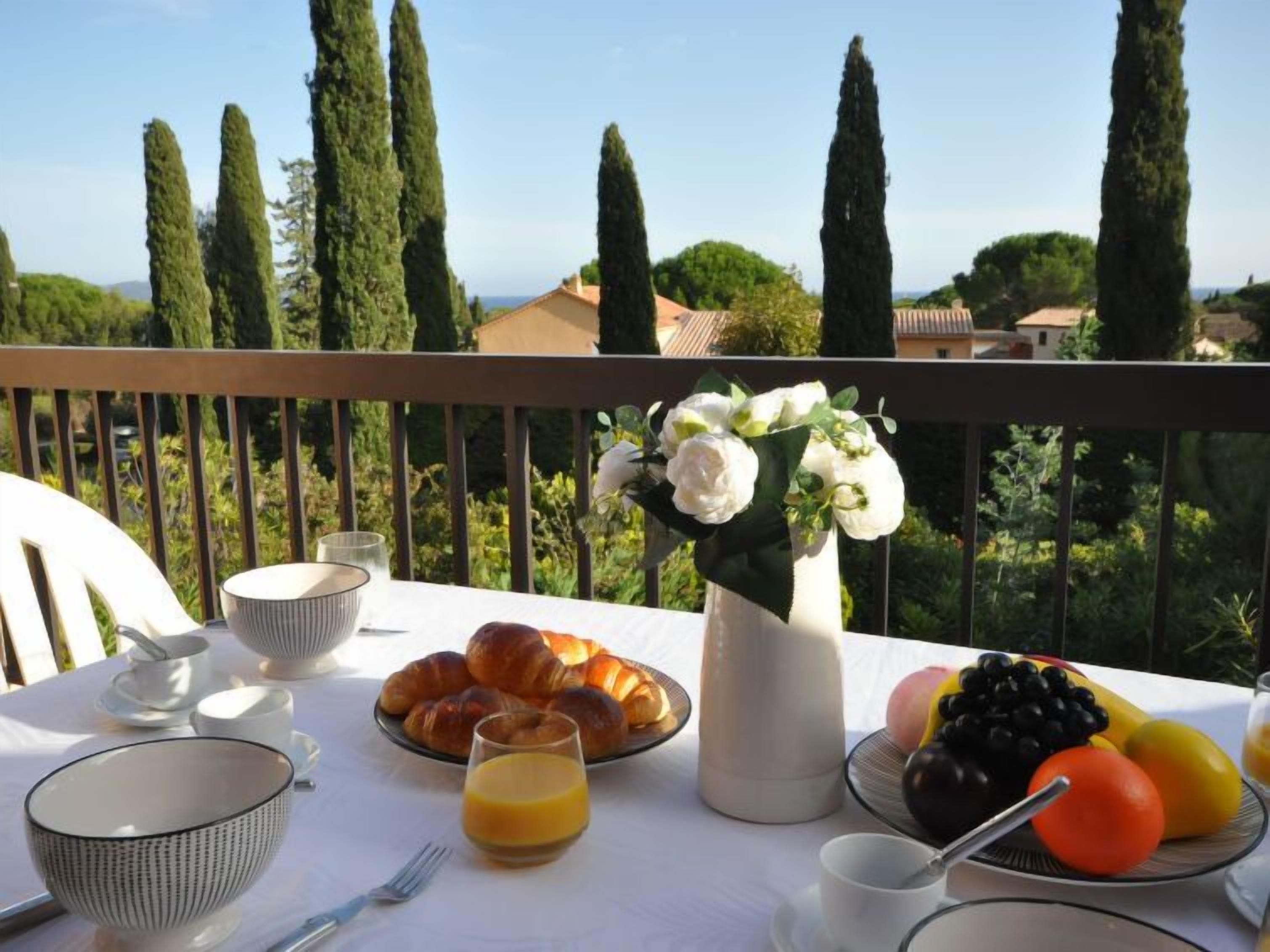 A breakfast setup on a balcony with croissants, fruit, and a vase of flowers.