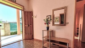 Un pasillo con una puerta de madera, un espejo, un jarrón con flores y un banco.