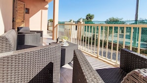 Un balcón con muebles de mimbre, vistas al mar y una cerca verde de malla.