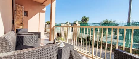 A balcony with wicker furniture, a view of the sea, and a green netted fence.