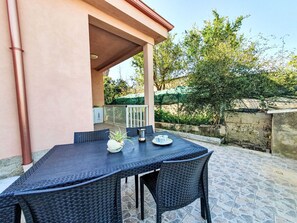 Eine Terrasse im Freien mit Tisch und Stühlen, einem Blumentopf und einem Metallbehälter.