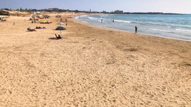 Una playa arenosa con sombrillas y gente.