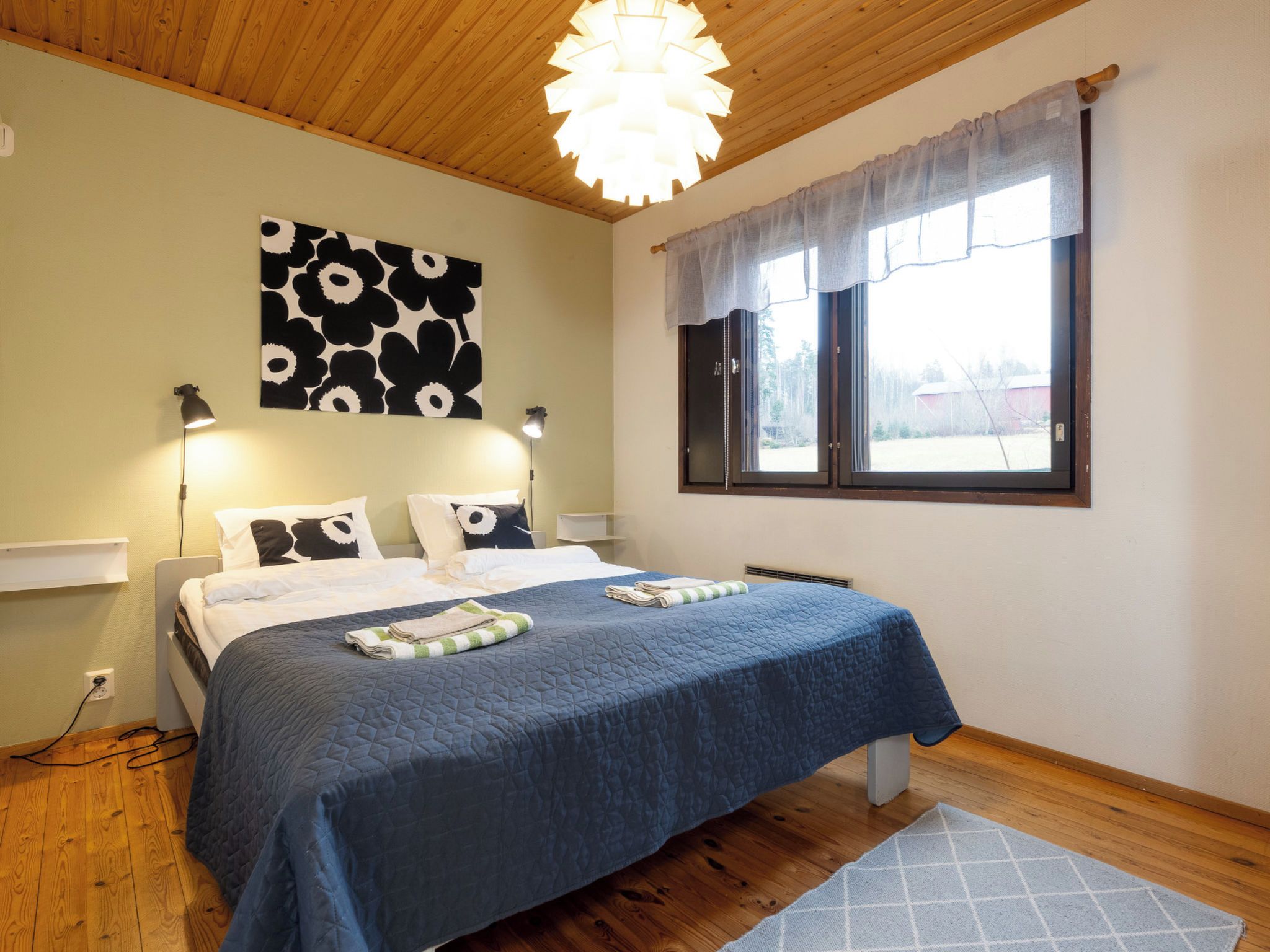 Un dormitorio con cama, lámpara de pared, ventana con cortinas e iluminación en el techo.