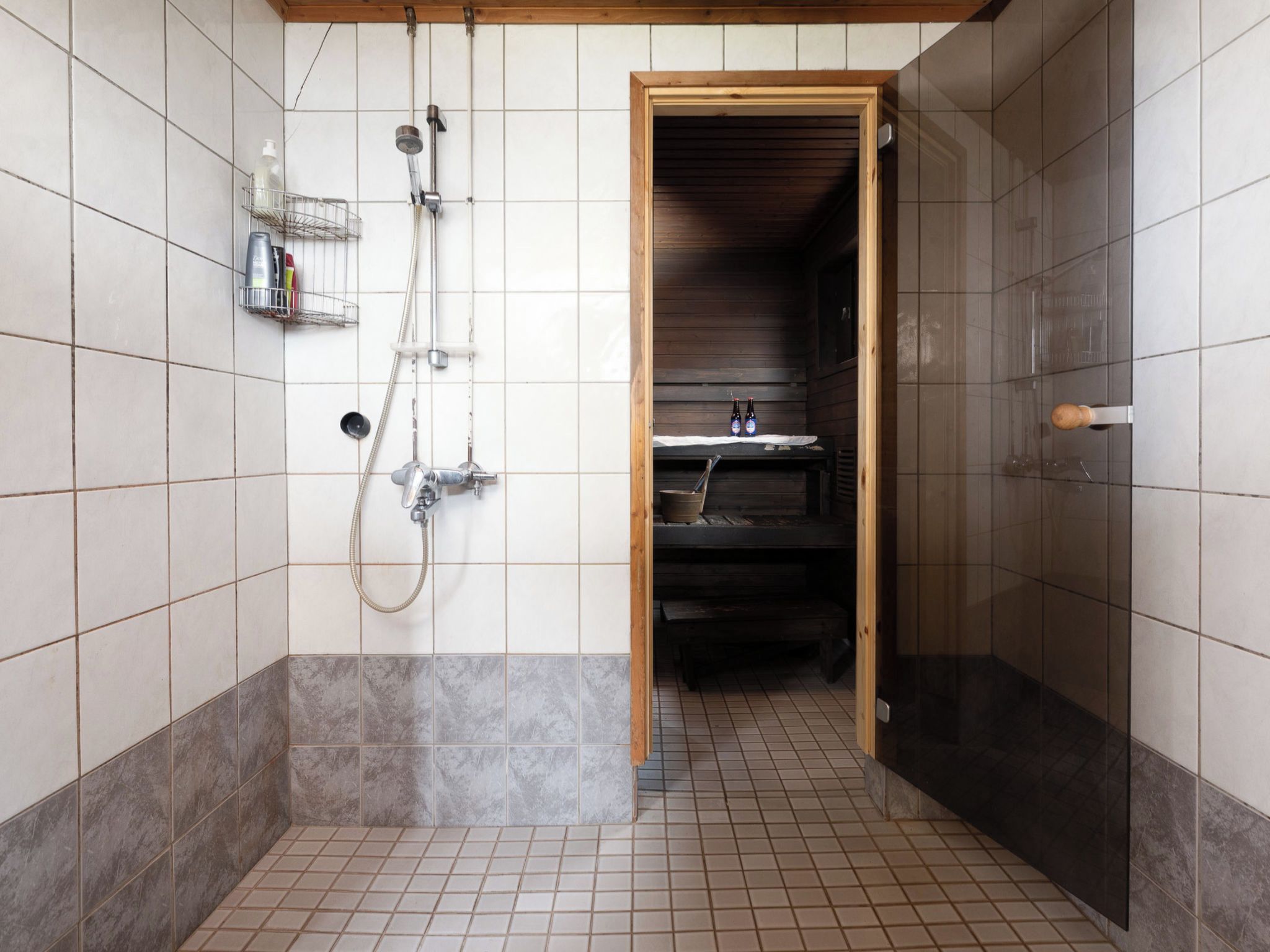 Een badkamer met een douche, een wastafel en een plank met toiletartikelen.