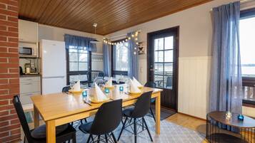 En mysig matplats med ett träbord dukat för fyra personer, omgivet av svarta stolar. Ett litet runt bord med ljus syns i hörnet.