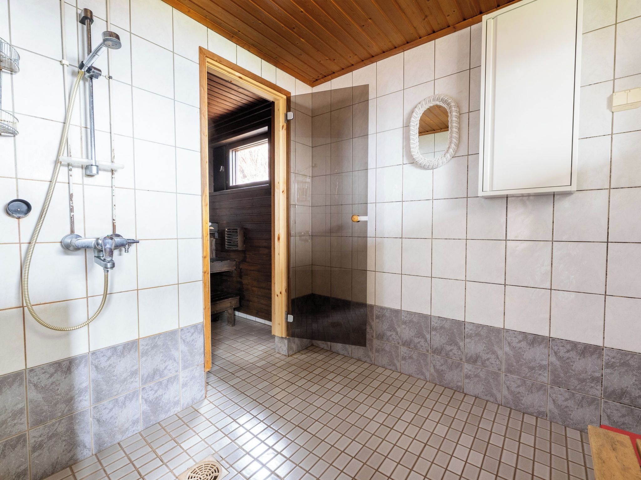 Une salle de bain avec une douche, un plafond en bois, des murs carrelés et une petite fenêtre.