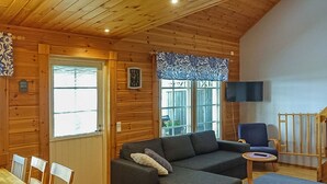 A cozy cabin interior with a wooden interior, a sofa, a dining table with chairs, and a television mounted on the wall. - Aallotar havina by Interhome (Paltamo)