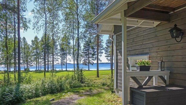 A wooden cabin with a porch overlooking a grassy area and a body of water. - Aallotar havina by Interhome (Paltamo)