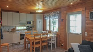 A cozy cabin-style kitchen with wooden walls, a dining table, and a window with a view. - Aallotar havina by Interhome (Paltamo)