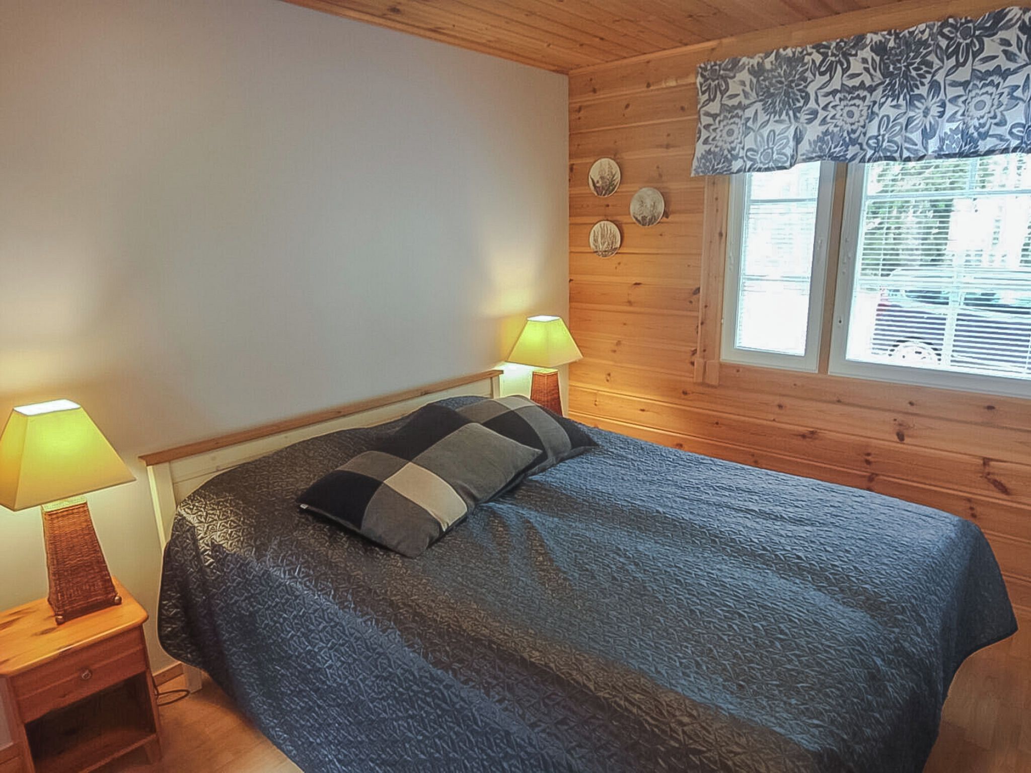 Una stanza con un letto, due lampade sui comodini, una finestra con persiane e una tenda decorata con motivi floreali.