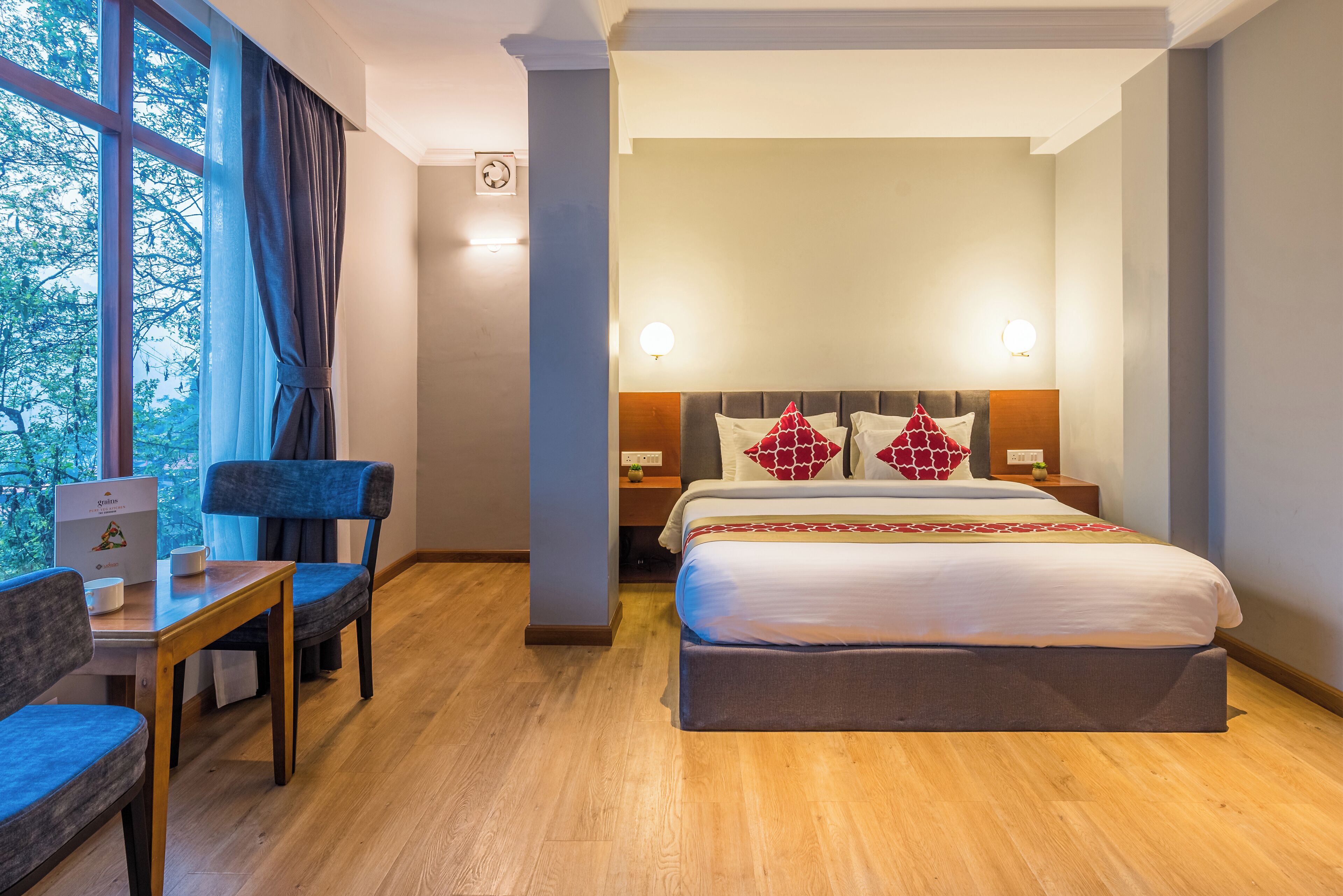 A hotel room with a large bed, bedside tables, a desk with a chair, and a window with curtains.