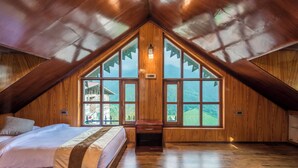 Une chambre avec un plafond en pente, des murs en bois, une grande fenêtre et un lit.