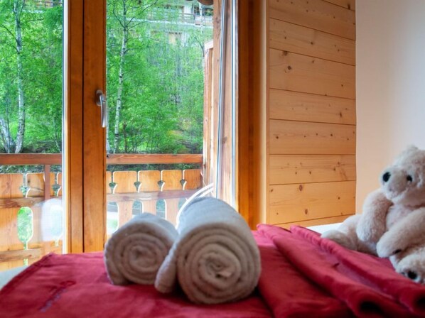 A room with a bed, a window with a view of trees, and a teddy bear on the bed.