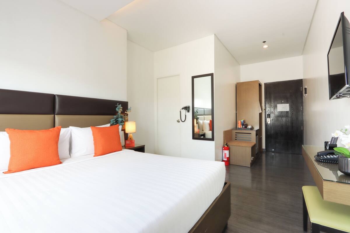 A hotel room with a large bed, a desk, a chair, a mirror, a wardrobe, and a television.