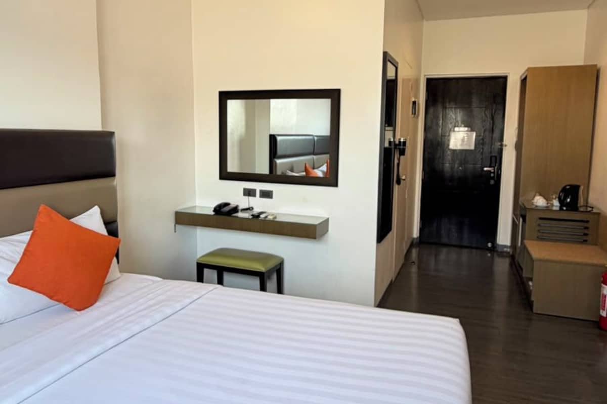 Una habitación de hotel con una cama grande, un escritorio, una silla, un espejo y un armario.