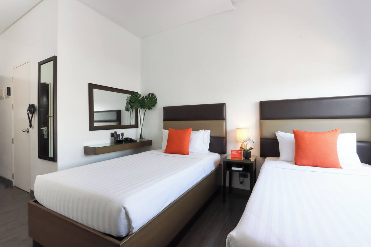 A hotel room with two beds, a nightstand, a mirror, and a small table with a lamp.