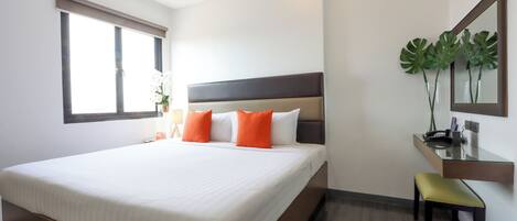 A hotel room with a large bed, a bedside table, a chair, a mirror, and a window with curtains.