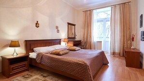 Een slaapkamer met een groot bed, houten nachtkastjes, een spiegel en uitzicht op het groen door een raam.