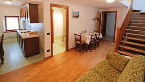Uma sala de estar espaçosa com piso de madeira, uma mesa de jantar posta para quatro pessoas e uma escada que leva a outro andar.