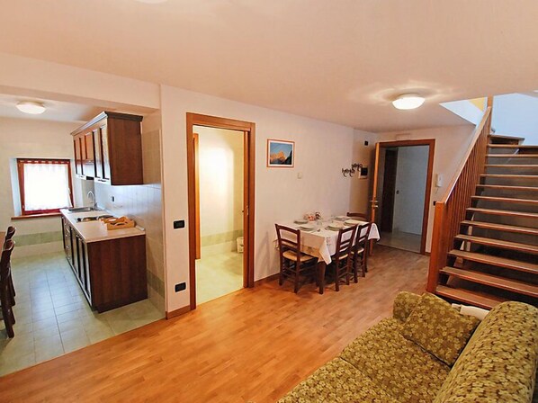 A spacious living area with a wooden floor, a dining table set for four, and a staircase leading to another level.