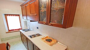 Uma cozinha com armários de madeira, bancada, pia e janela com cortina vermelha.