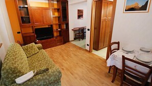 Uma sala de estar com sofá, rack de TV e área de jantar com cadeiras e mesa.