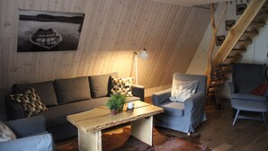 A cozy living room with a wooden sloped ceiling, a sofa, a chair, a coffee table, and a staircase. - Äventyrscampen in Sövde (Sjobo)