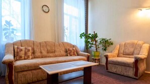 Un salon avec un canapé, un fauteuil et une table basse. On y trouve une plante en pot et une horloge au mur.