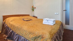 Un lit bien fait, avec une couverture marron et un coussin décoratif, un vase rempli de fleurs et une pile de serviettes pliées sur la table de chevet.