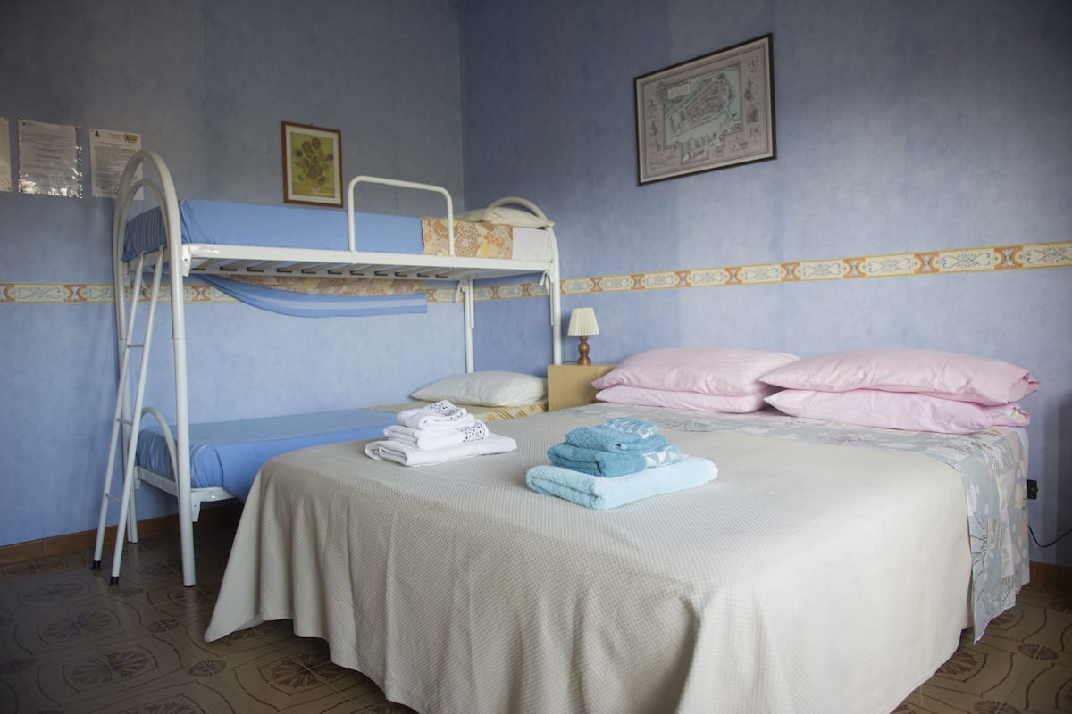 A bunk bed room with a blue wall, a patterned border, a bed with white and pink bedding, and a ladder.