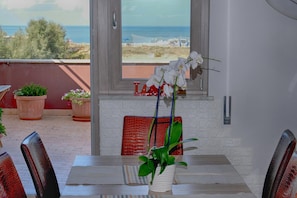 A dining table with a potted plant, a red cushion, and a view of the sea through a window. - BB Fly and Beach (Fiumicino)