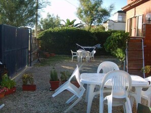 A patio with white plastic chairs and a table, surrounded by potted plants and a gravel ground. - BB Fly and Beach (Fiumicino)
