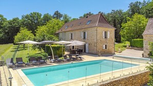 Ein Steinhaus mit Swimmingpool, Außenbereich mit Sitzgelegenheiten und einem gepflegten Rasen.