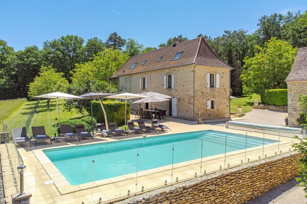 Ein Steinhaus mit Swimmingpool, Außenbereich mit Sitzgelegenheiten und einem gepflegten Rasen.