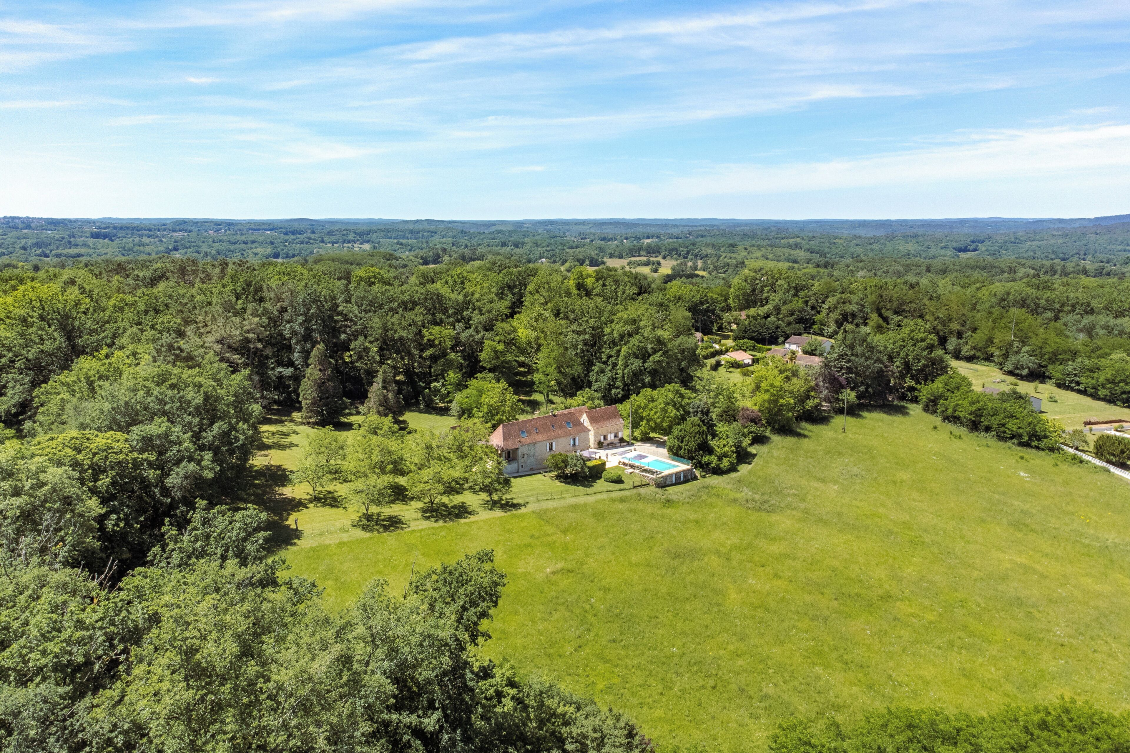 Une grande maison entourée d’une forêt dense, avec une piscine bien visible et une pelouse bien entretenue.
