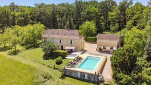 Une grande maison avec une piscine, entourée d’une végétation luxuriante et d’arbres.