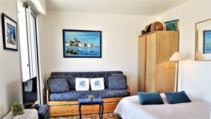 Une pièce confortable avec un canapé, un lit, une armoire en bois et un tableau représentant un paysage côtier.