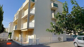 Un immeuble résidentiel à plusieurs étages, doté de balcons, d’une entrée sécurisée et d’une voiture garée.