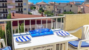 Un balcon avec une table dressée pour deux personnes, donnant sur un quartier résidentiel et la mer.
