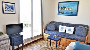 Un salon avec un canapé, un téléviseur, une petite table et un balcon offrant une vue agréable.