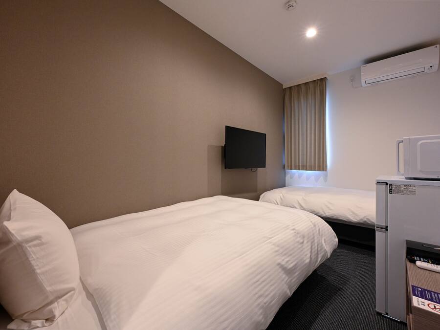 Habitación de hotel con dos camas individuales, un televisor de pantalla plana montado en la pared, un minibar y un equipo de aire acondicionado.