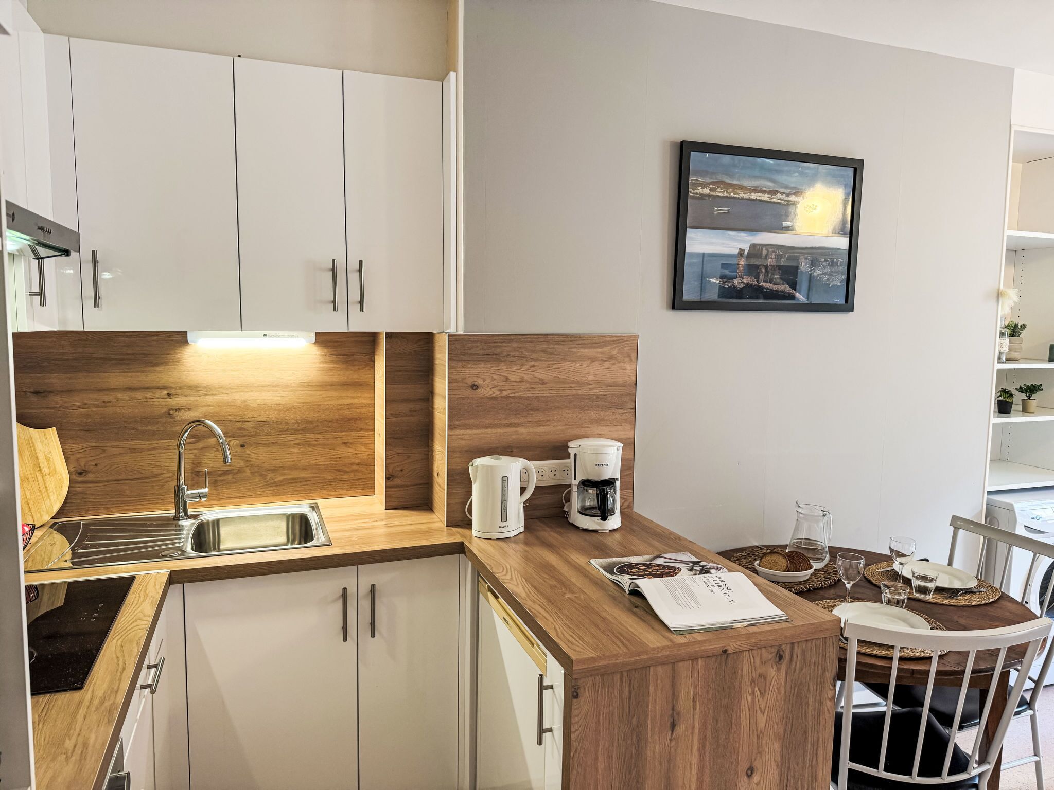 A compact kitchen with a wooden countertop, a coffee maker, and a dining area with a table set for two.