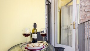 A table with a bottle of wine, two glasses, and a plate of food on a balcony.