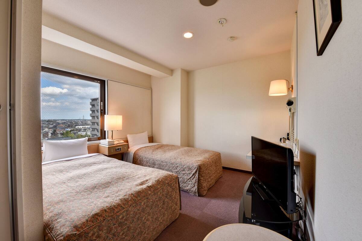 Une chambre d’hôtel avec deux lits, une télévision, une lampe et une fenêtre donnant sur la ville.