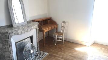 Una habitación con chimenea, un banco de madera, una silla y un ventilador.