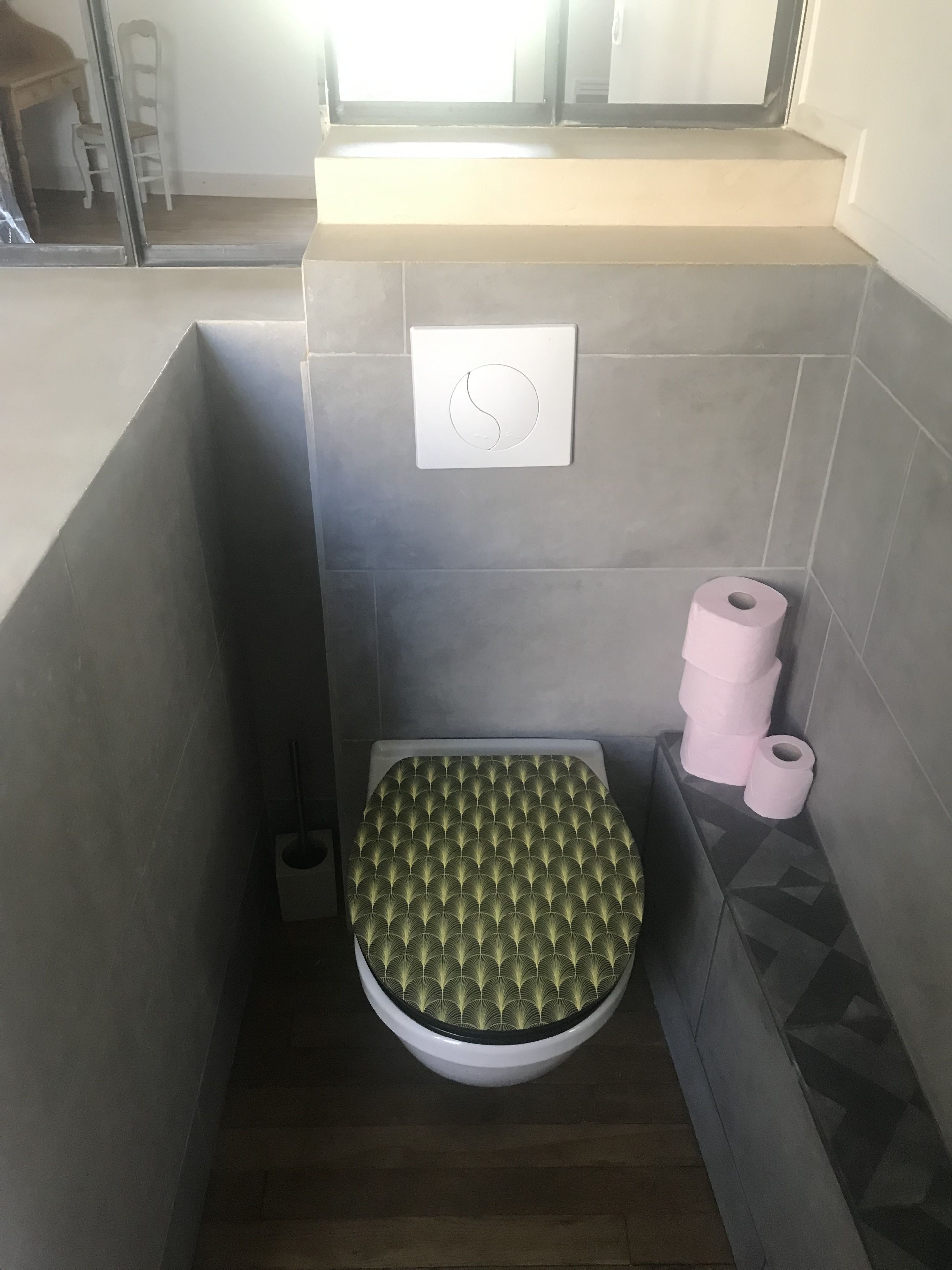 Un baño pequeño y moderno con inodoro, soporte para papel higiénico y un interruptor de luz en la pared.